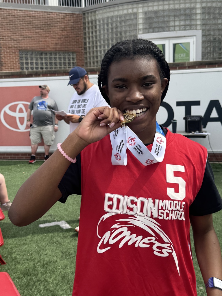Girl with braided hair holds a gold medal, wearing a red Edison Middle School jersey, smiling.