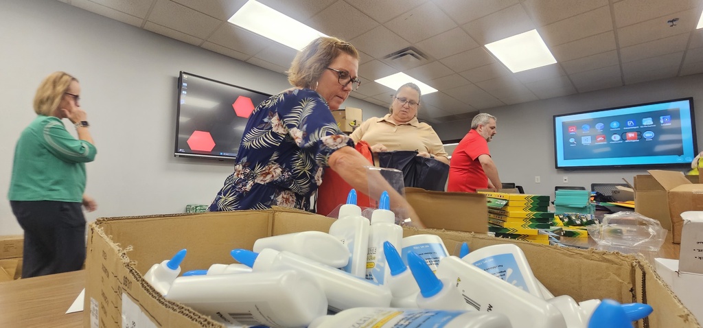 A group of people in a room with a large box of cleaning products on a table.