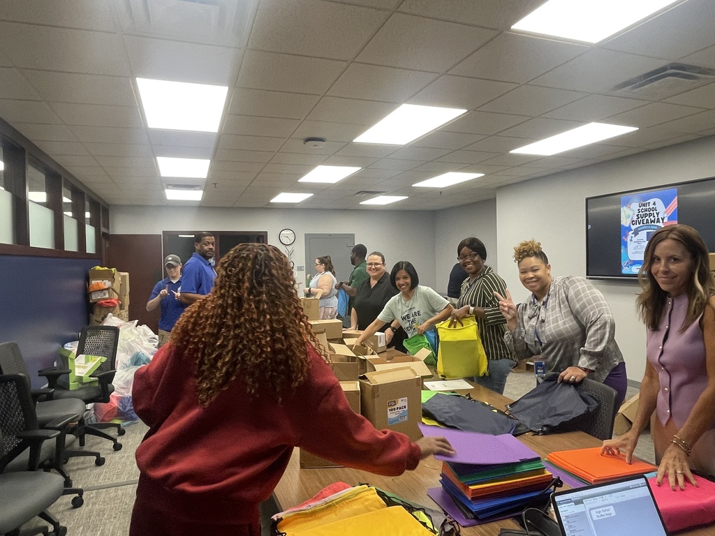 People in a room with a table filled with colorful papers and bags, working together.