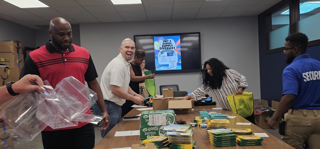 A group of people in a room, standing around a table with boxes, bags, and other items.