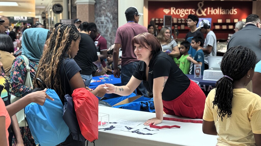A woman in a red skirt helps others at a table in a crowded mall with a Rogers & Hollands sign.