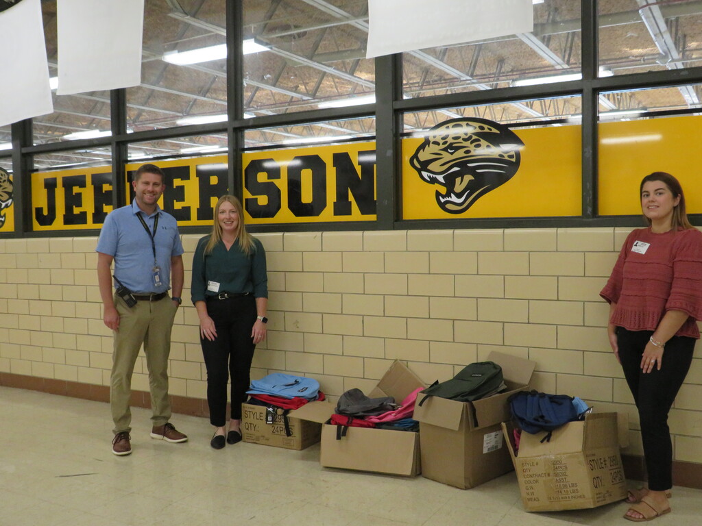 Three people stand near a brick wall. A yellow banner with the word Jefferson and a logo is behind them.