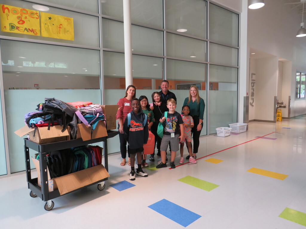 People stand in a hallway, smiling for a photo. Behind them, boxes and bags are on a cart.