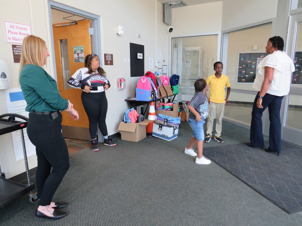 A group of adults and children in a room. One adult is gesturing. Two children are standing.