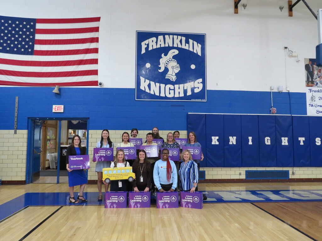 Group in a gym with "Franklin Knights" on wall. American flag in background. Holding purple boxes.