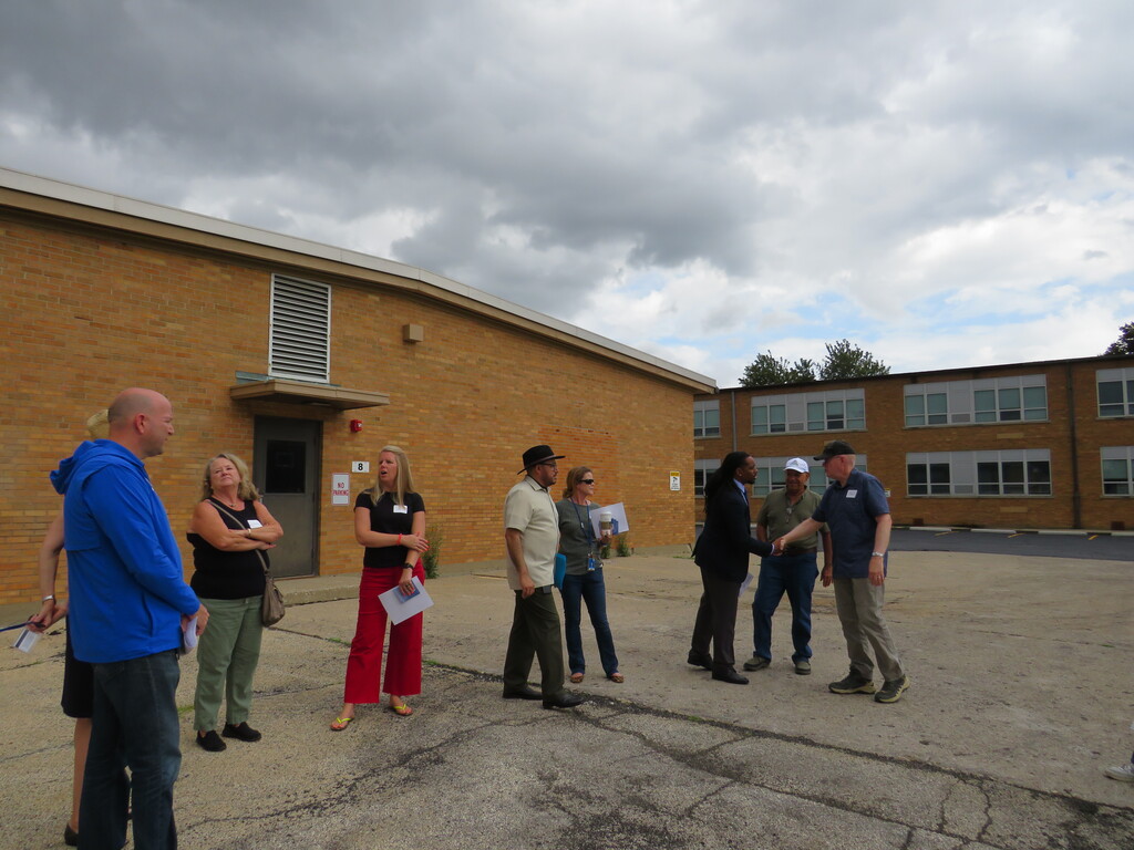 Several people stand in a line in front of a brick building with a cloudy sky.