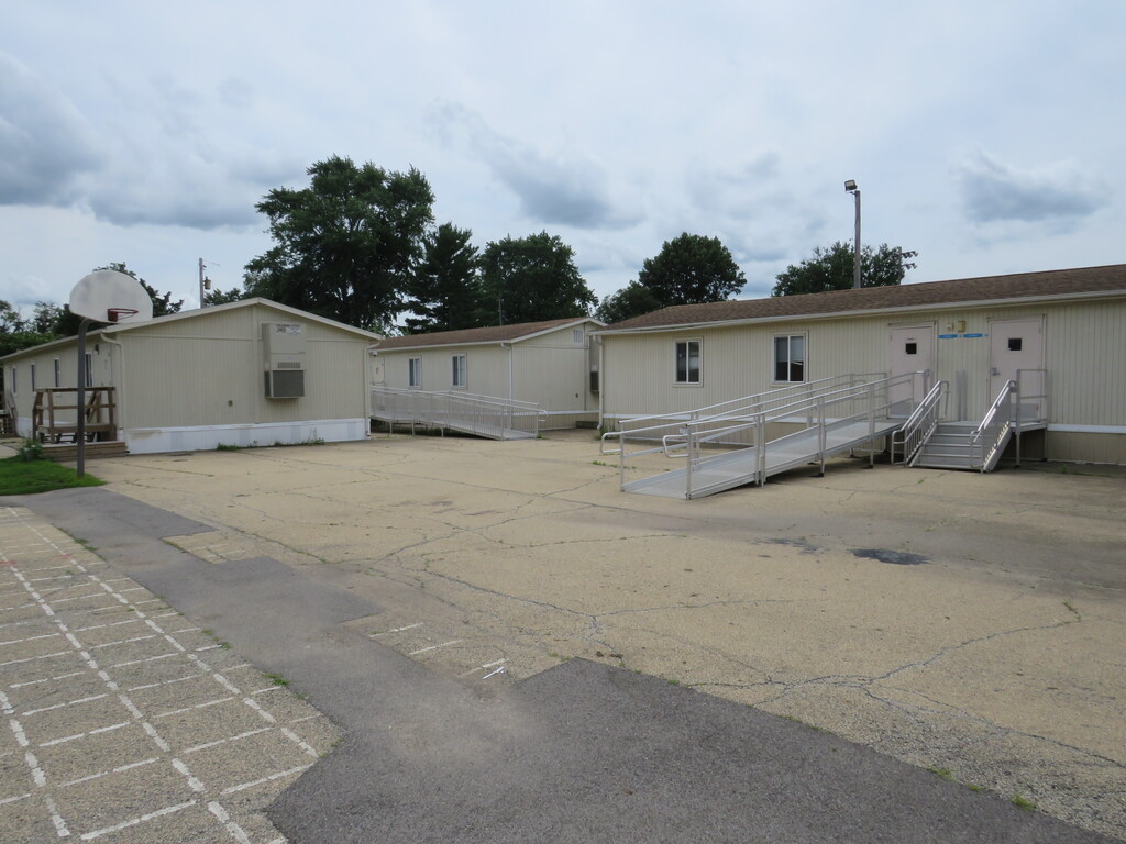 Three small buildings line an empty parking lot. A basketball hoop is next to the building on the left.