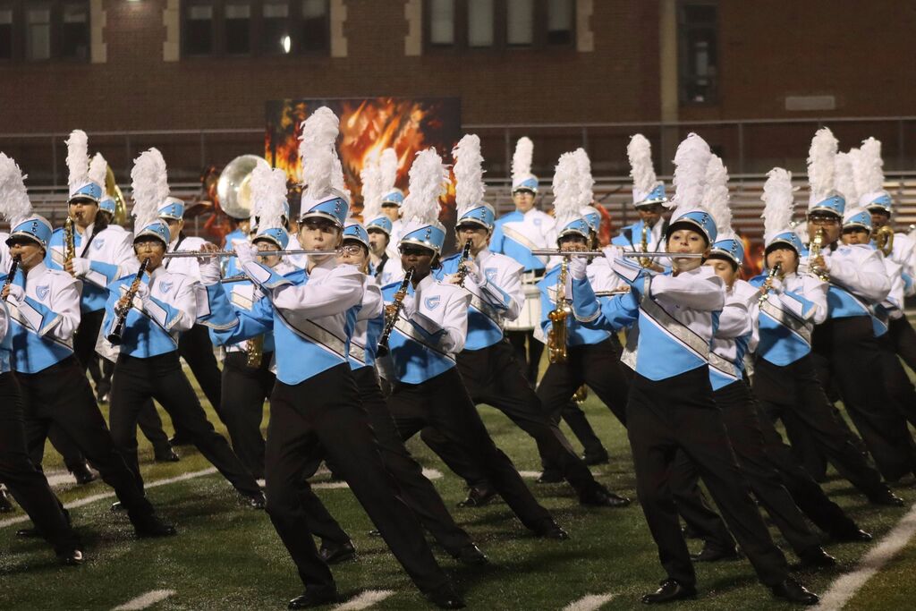 Centennial High School marching band performs on a field with blue and white uniforms. They play brass and woodwind instruments.