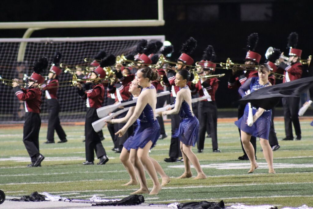 Champaign Central High School marching band performs on a field. Students play instruments while the color guard wears blue dresses and dance with white props.