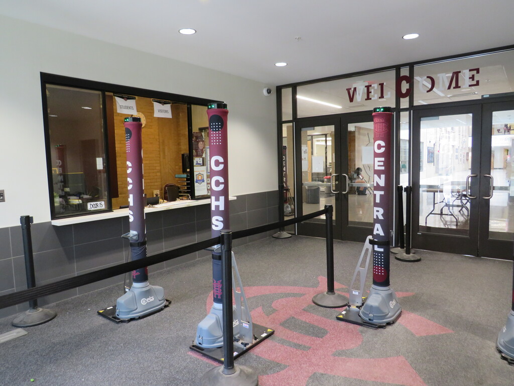 A hallway with a glass door labeled Central at the end. Red poles with a black rope barrier are lined up in front.