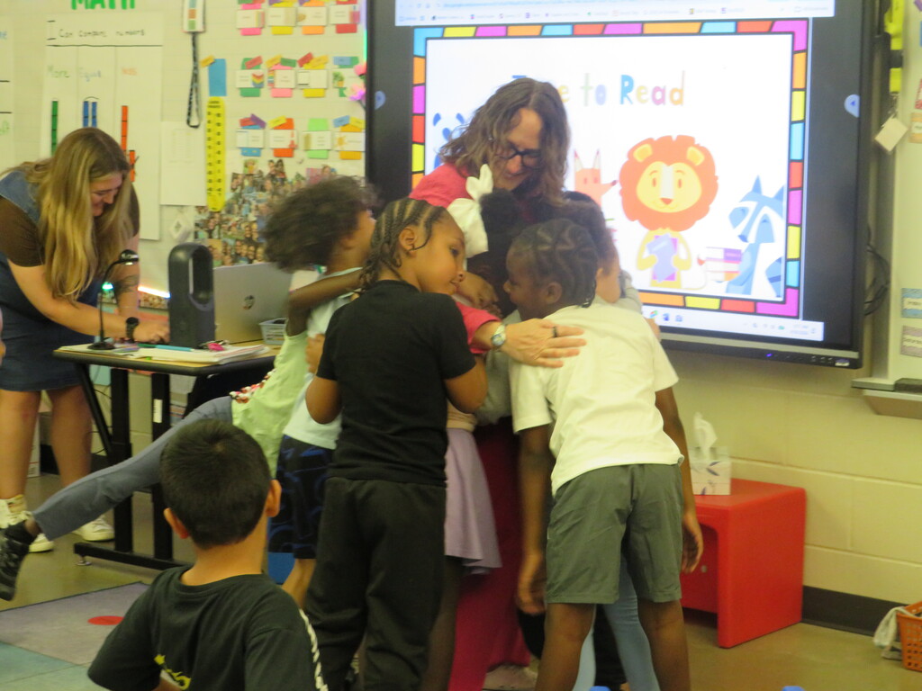 A classroom with children and an adult. A large screen shows an image of a lion.