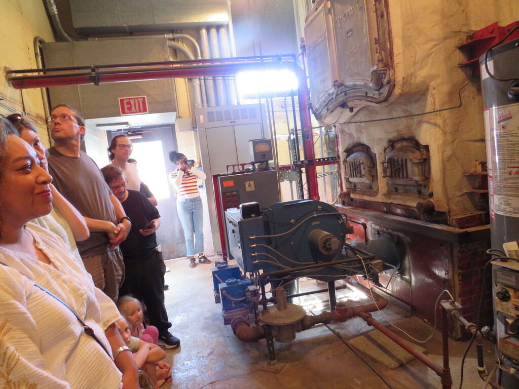 A group of people examine machinery in a factory setting, with one person wearing a white shirt.