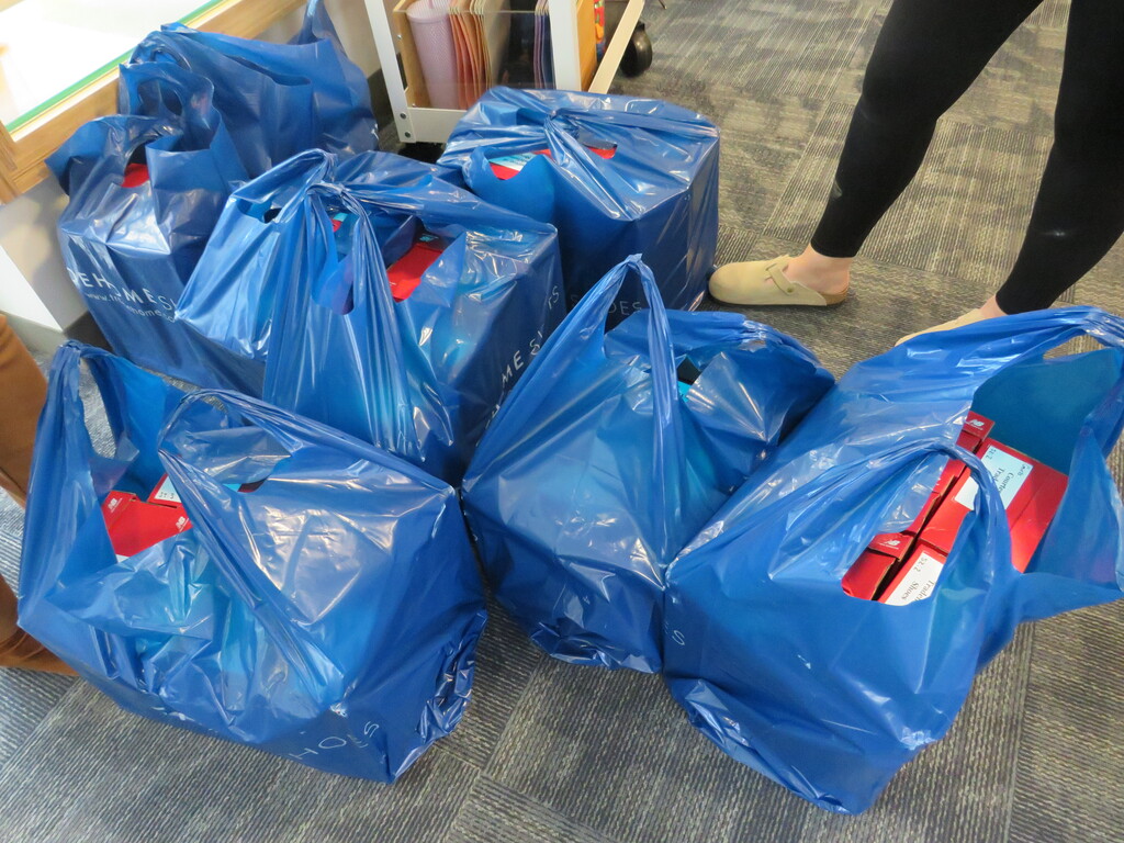 Several blue plastic bags filled with various items are lined up on the floor. A person wearing black pants and a yellow shoe is standing nearby.