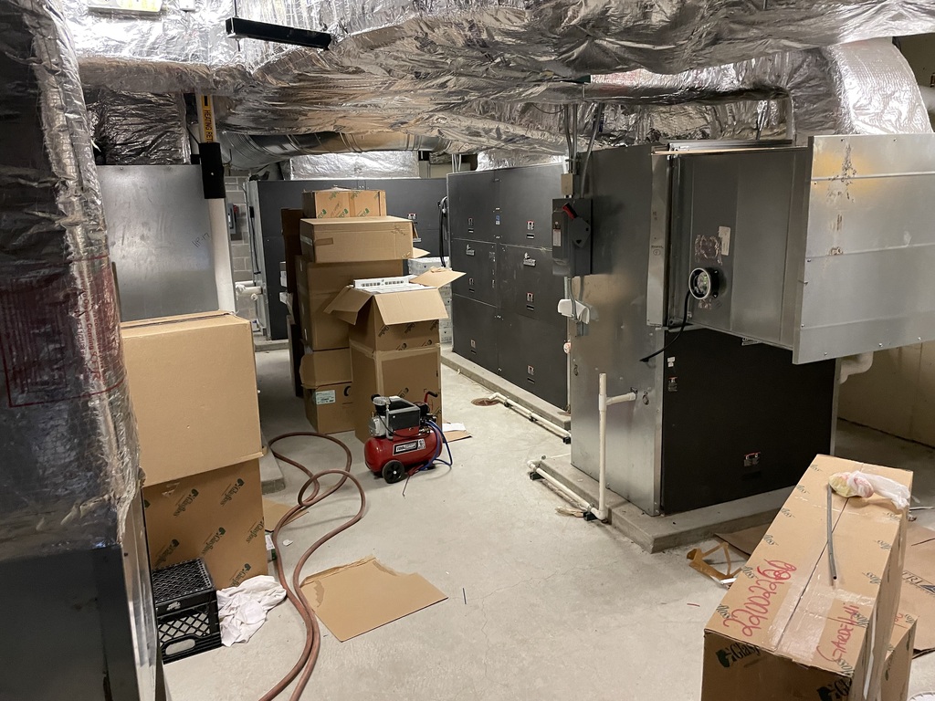 A room with boxes stacked up and a large metal air conditioning unit covered with plastic wrap.