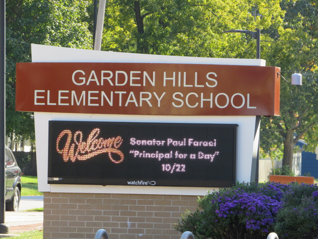 Garden Hills Elementary School sign with a digital message. Purple flowers in front. Trees and greenery behind.