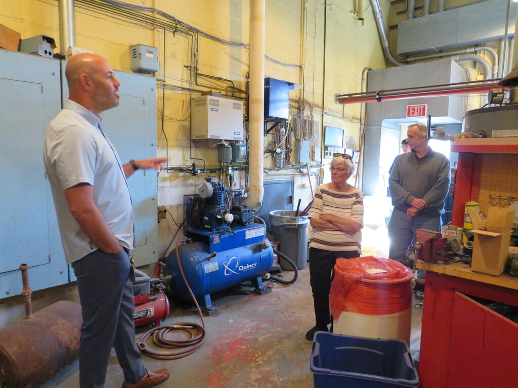 People in a room with industrial equipment. One person speaks with a hand gesture.