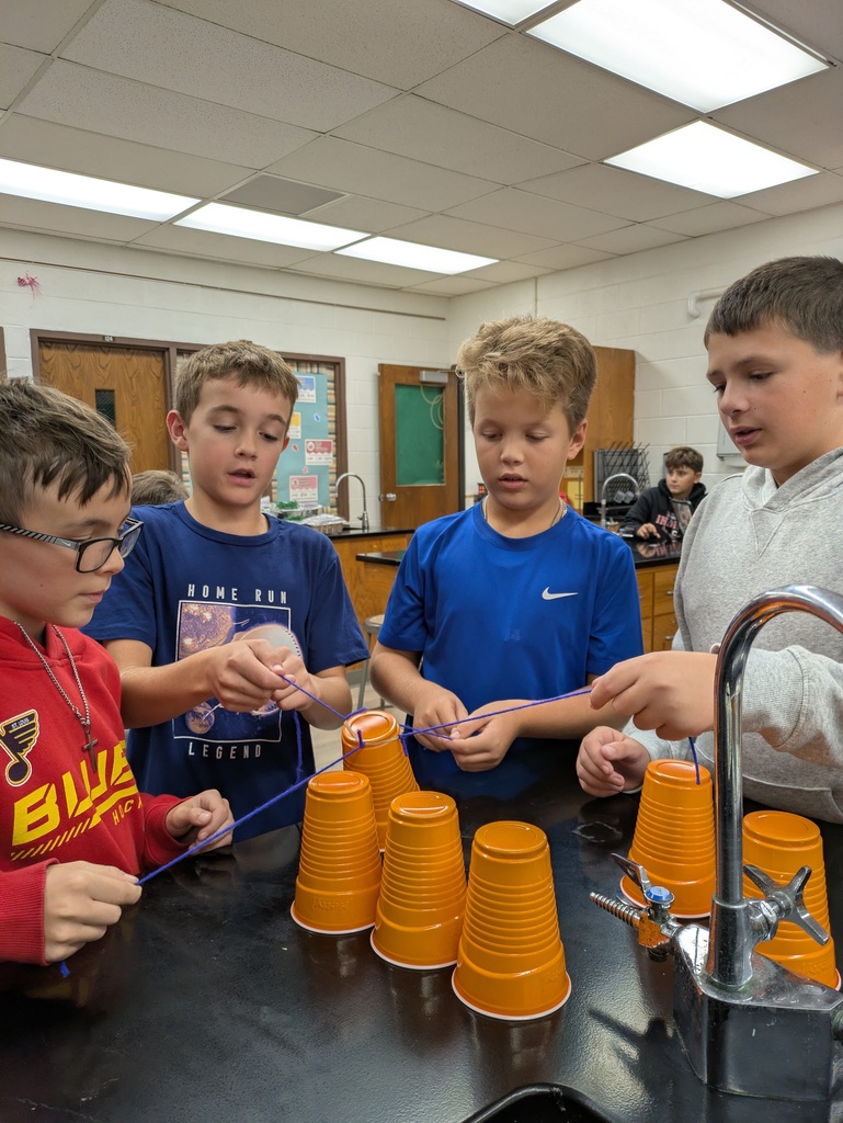 Students with cups and rubber bands trying to pick up cup