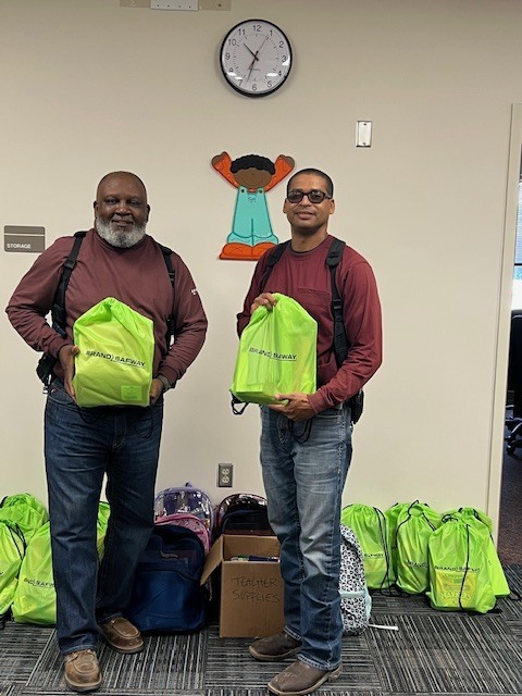 Pictured are Charles Byrd and Nestor Benavides holding green backpacks filled with school supplies. 