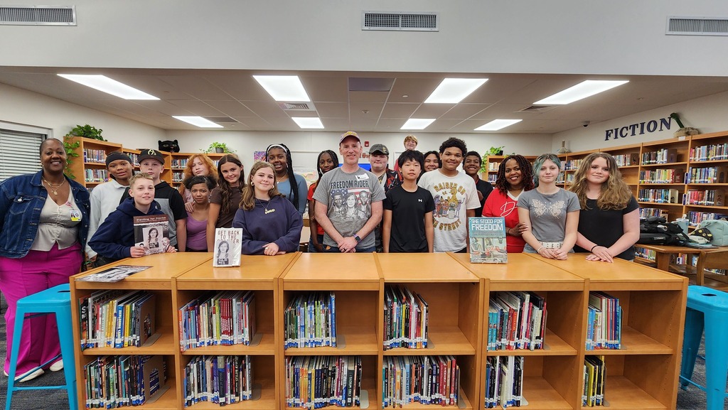 A group of students and three adults standing in a library
