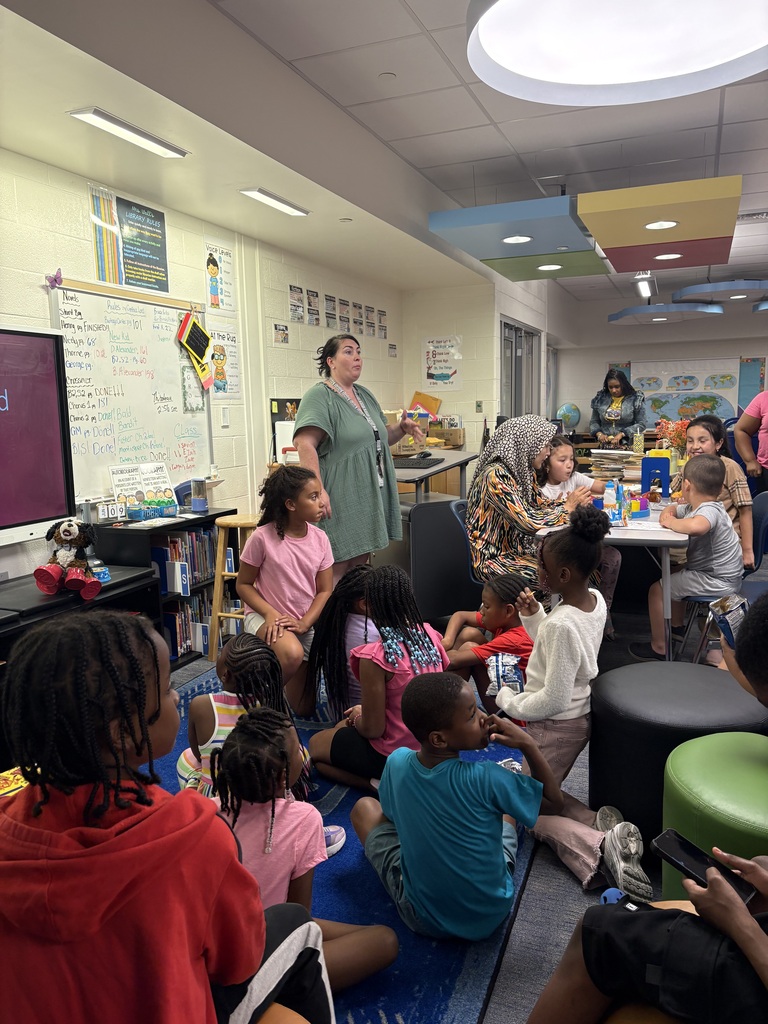 Families and students gather in the Dr. Mudd Elementary media center during 2nd Grade Transition Night. Third grade teachers speak with families and provide information about classroom expectations, academic programs, and the transition from 2nd to 3rd grade. Students sit and listen while families engage in discussions and ask questions about the upcoming school year. 