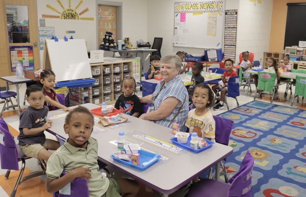 Pre-K students sit at classroom tables with their teacher while enjoying a first-day breakfast.