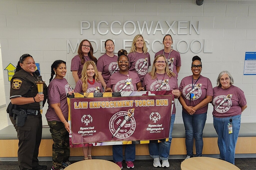 school resource officer and staff members wearing Torch Run tshirts and holding the torch run banner