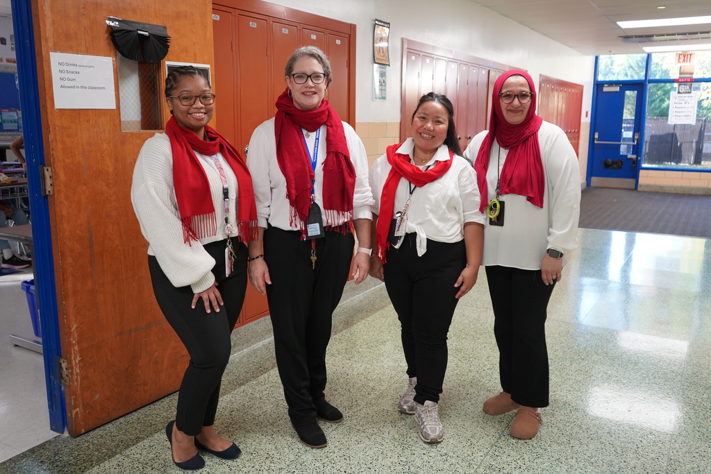 Four teachers standing, wearing white shirts and red scarves.