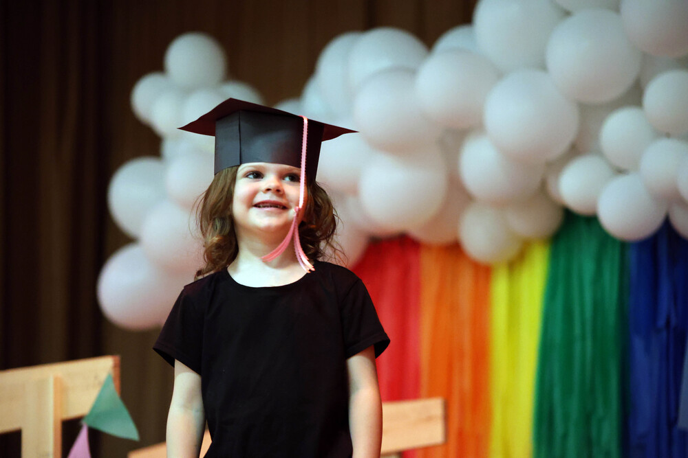 girl wearing graduation cap stnding in front of rainbow backdrop