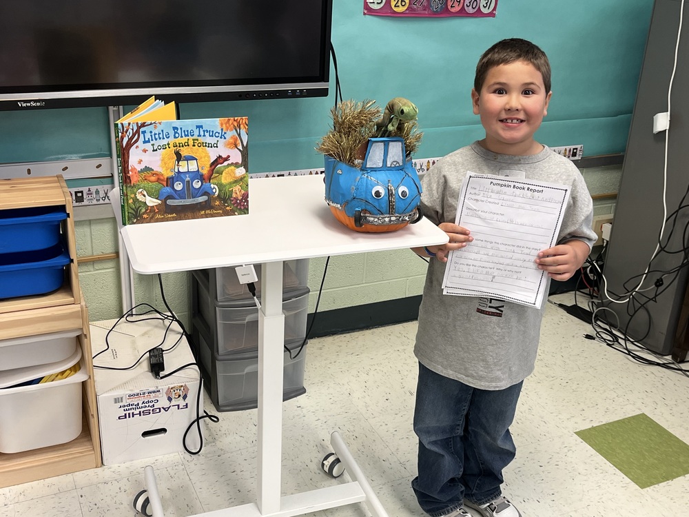 boy posing with book, book report, and pumkin decorated like a pickup truck
