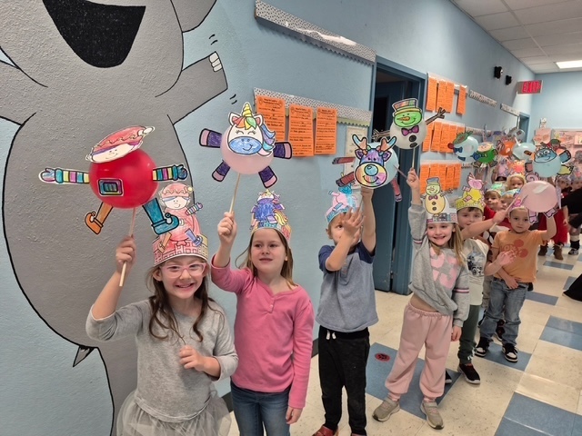 students holding baloons decorated as creatures and walking down the school hallway