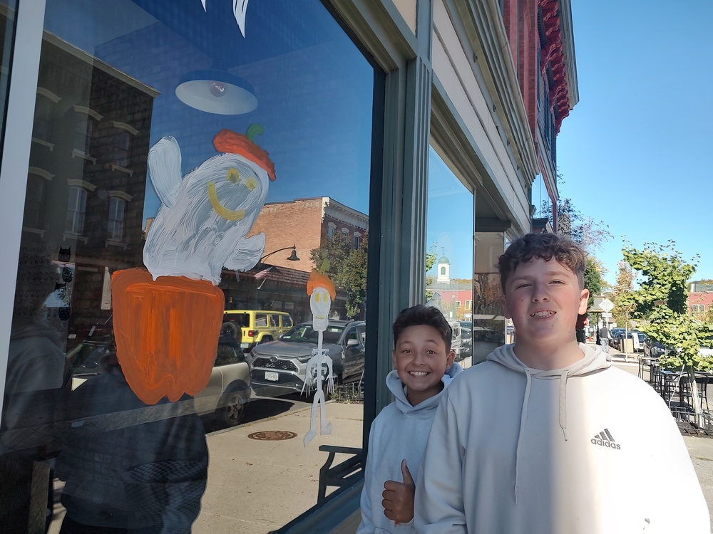 boys posing with window painted with skelton and ghost popping out of pumkin