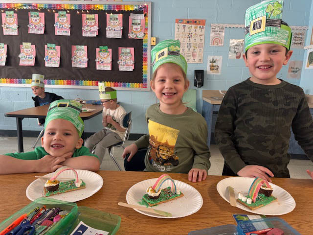 three students with rainbow shaped cookies wearing leprechaun hats