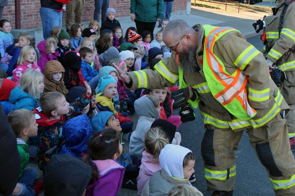 firefighter giving high five to boy seated in crowd of children