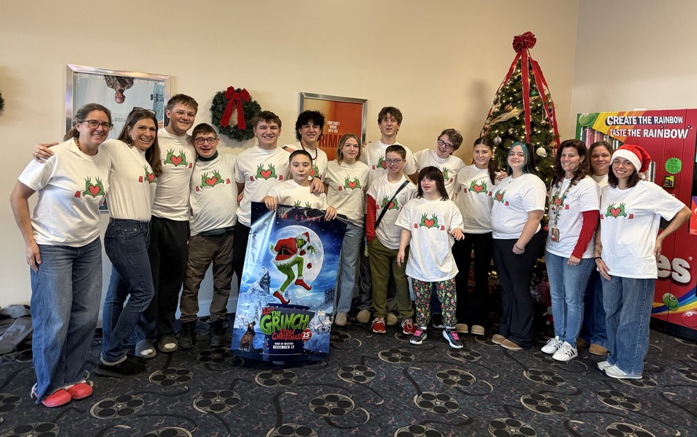 group photo of high schoolers and adults wearing Grinch t-shirts standing in movie theatre lobby