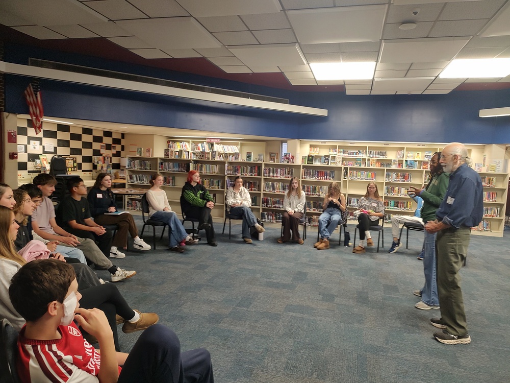 students seated in circle listening to two adults