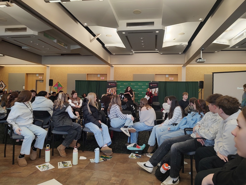 students listening to presenter in large room full of people. 