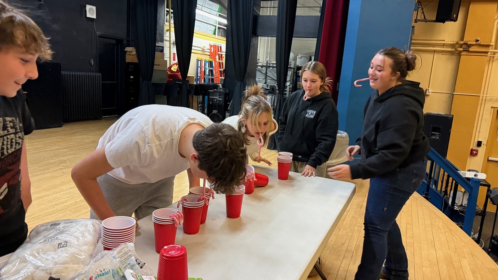 student with candy canes in their mouths trying to pick up candy canes in cups