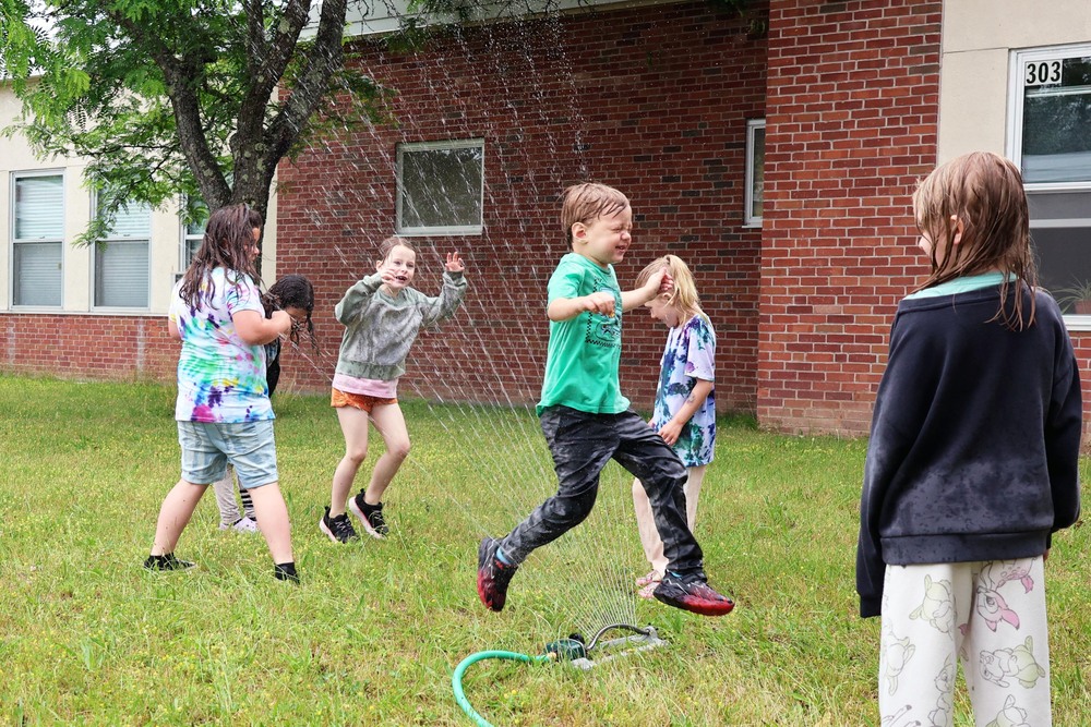 students running through sprinkler in school courtyard