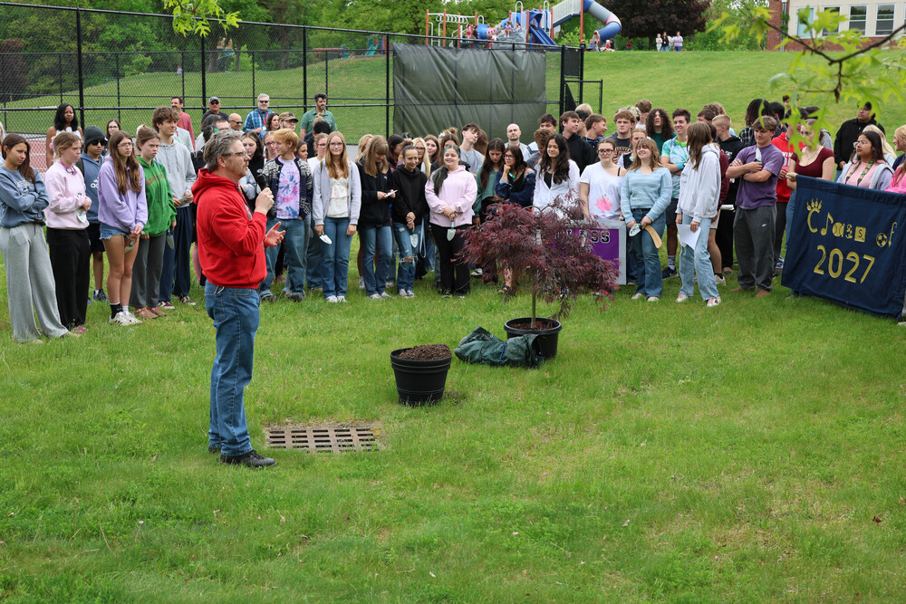 man talking to students gather around small tree in pot