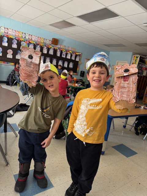 two boys wearing paper crowns and holding paper-bag groundhog puppets