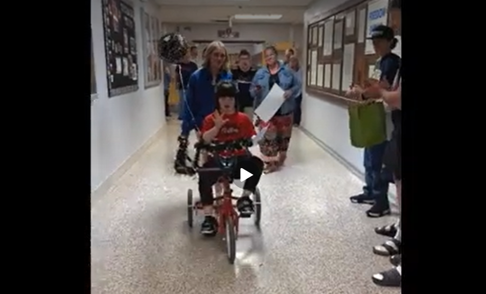 girl riding tricycle through school hallway filled with applauding students and staff