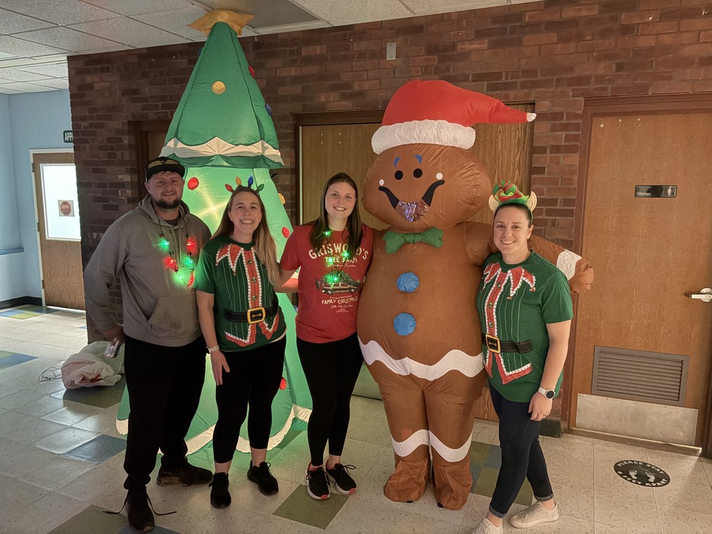three women and man pose with tree and gingerbread man blow ups