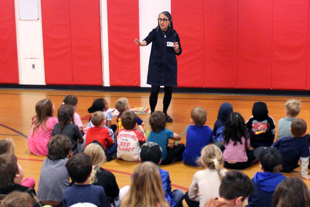 Woman speaking to group of children seated on gym floor