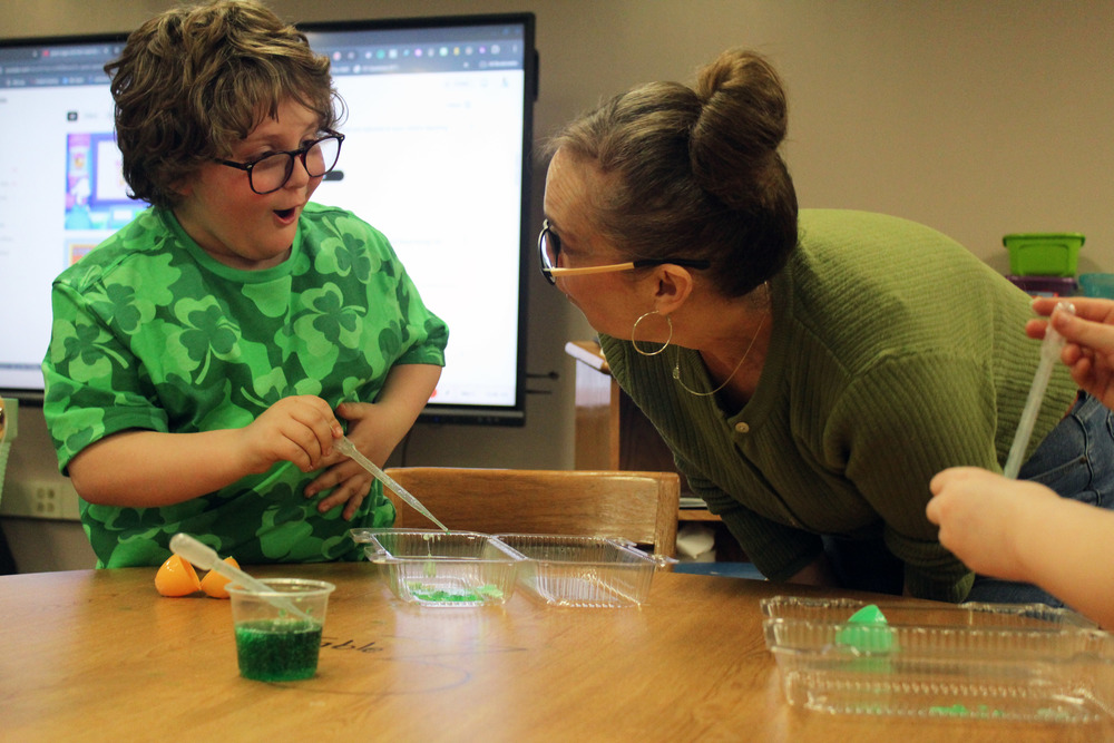 boy smiling and holding dropper with green liquid in it.