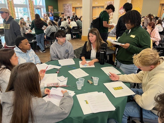 students seated around table in large college room.
