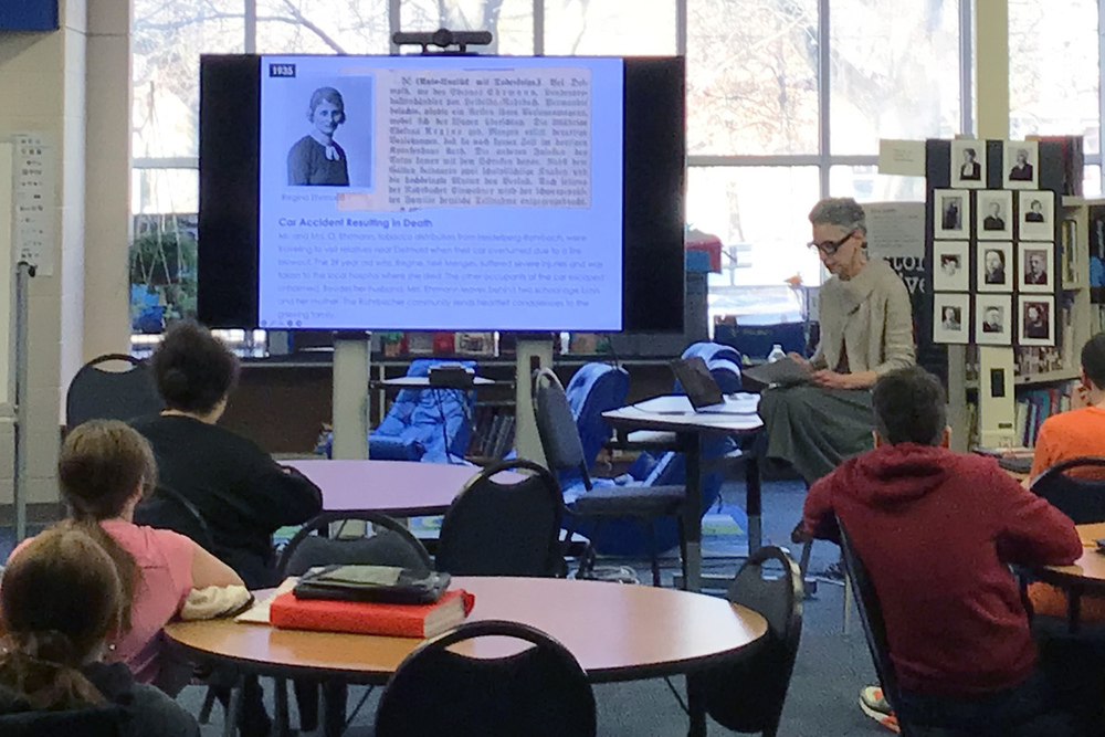 woamna reading from letter in front of students seated at tables