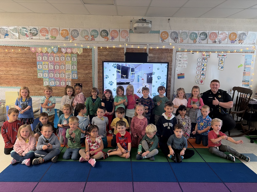 class of young children pose for group photo with sheriff's deputy.