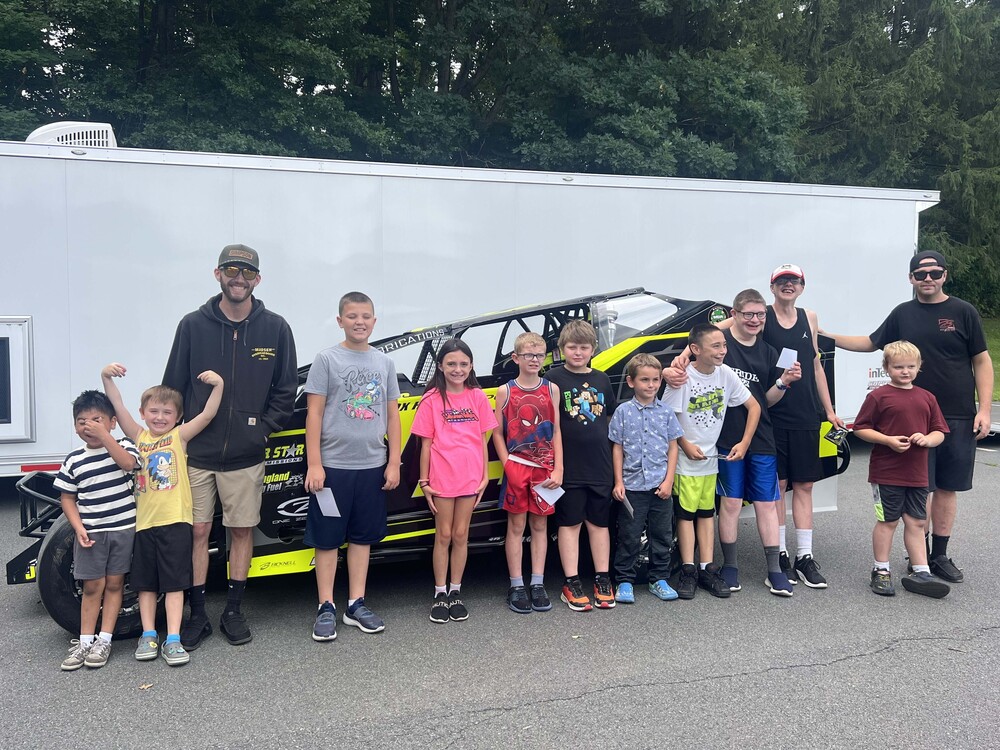 students and race car drivers standing around race car