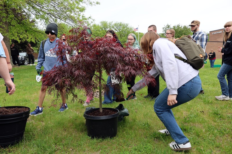 student shovel scoops of dirt onto small tree in pot