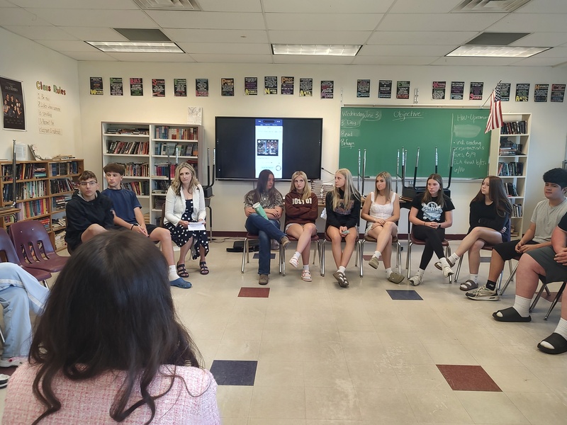 students sitting in circle listening to woman talk
